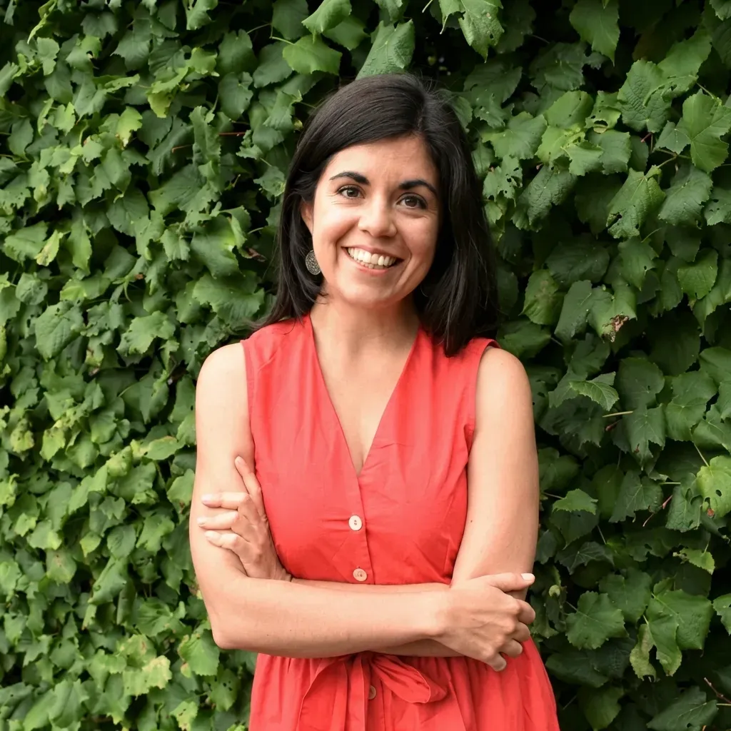 Carmen smiling with arms crossed in front of green ivy