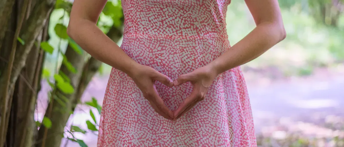 Carmen making a heart shape with hands over belly in nature