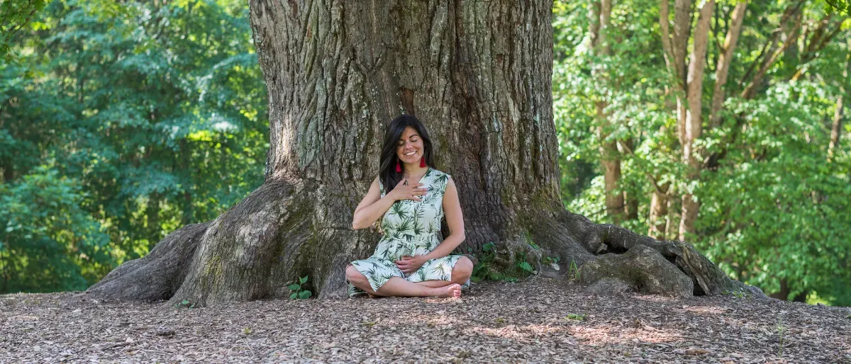 Carmen sitting peacefully at the base of a large tree in nature