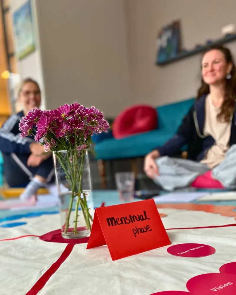Women gathering in a workshop circle with flowers and menstrual phase cards