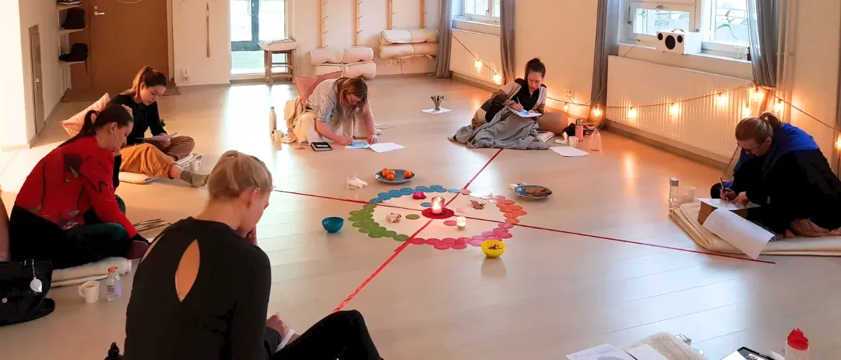 Women gathered in a circle at a workshop, journaling and connecting around a menstrual cycle wheel